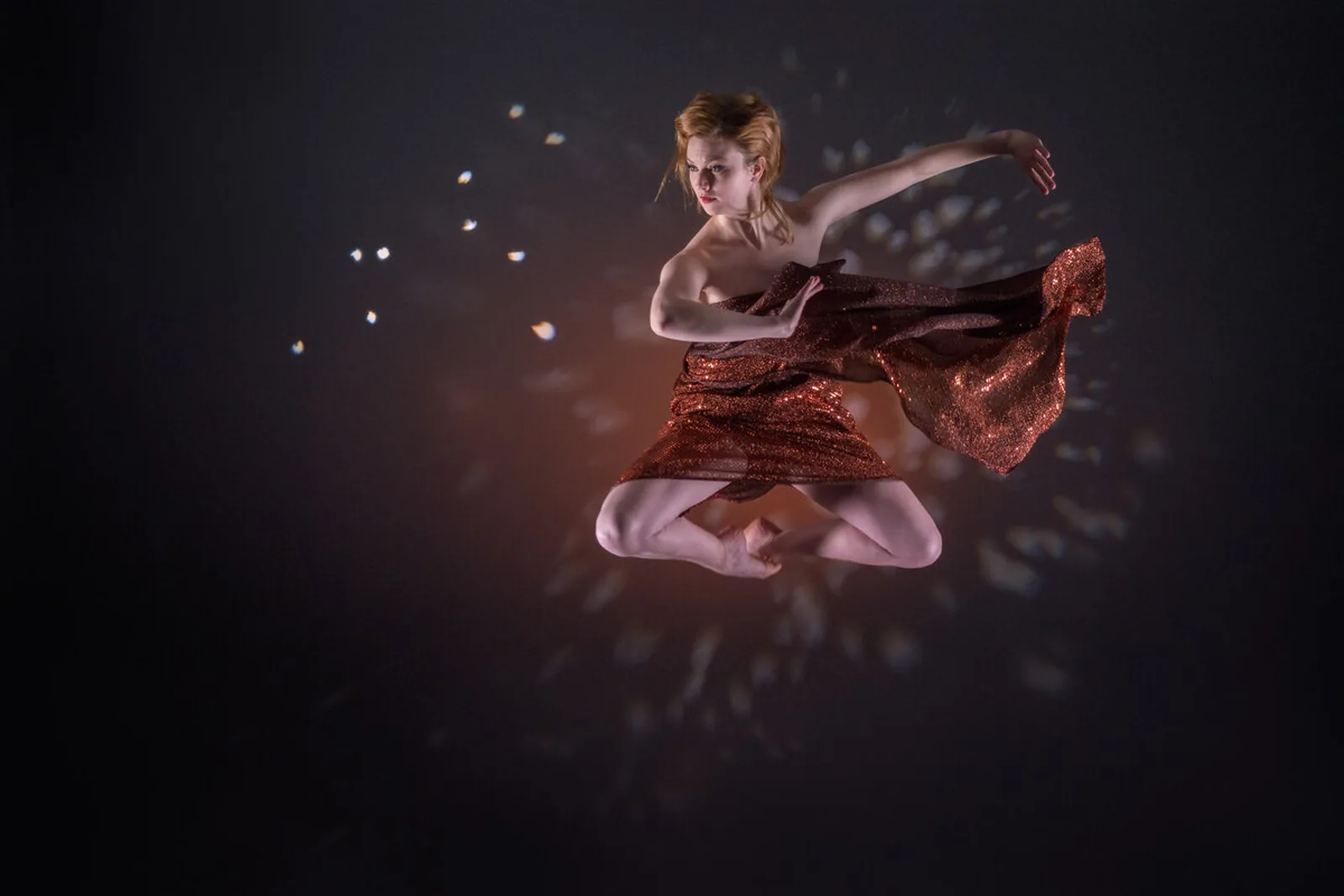 A dancer suspended mid-air in a studio, a length of red fabric unfurling behind her against a dark ground.